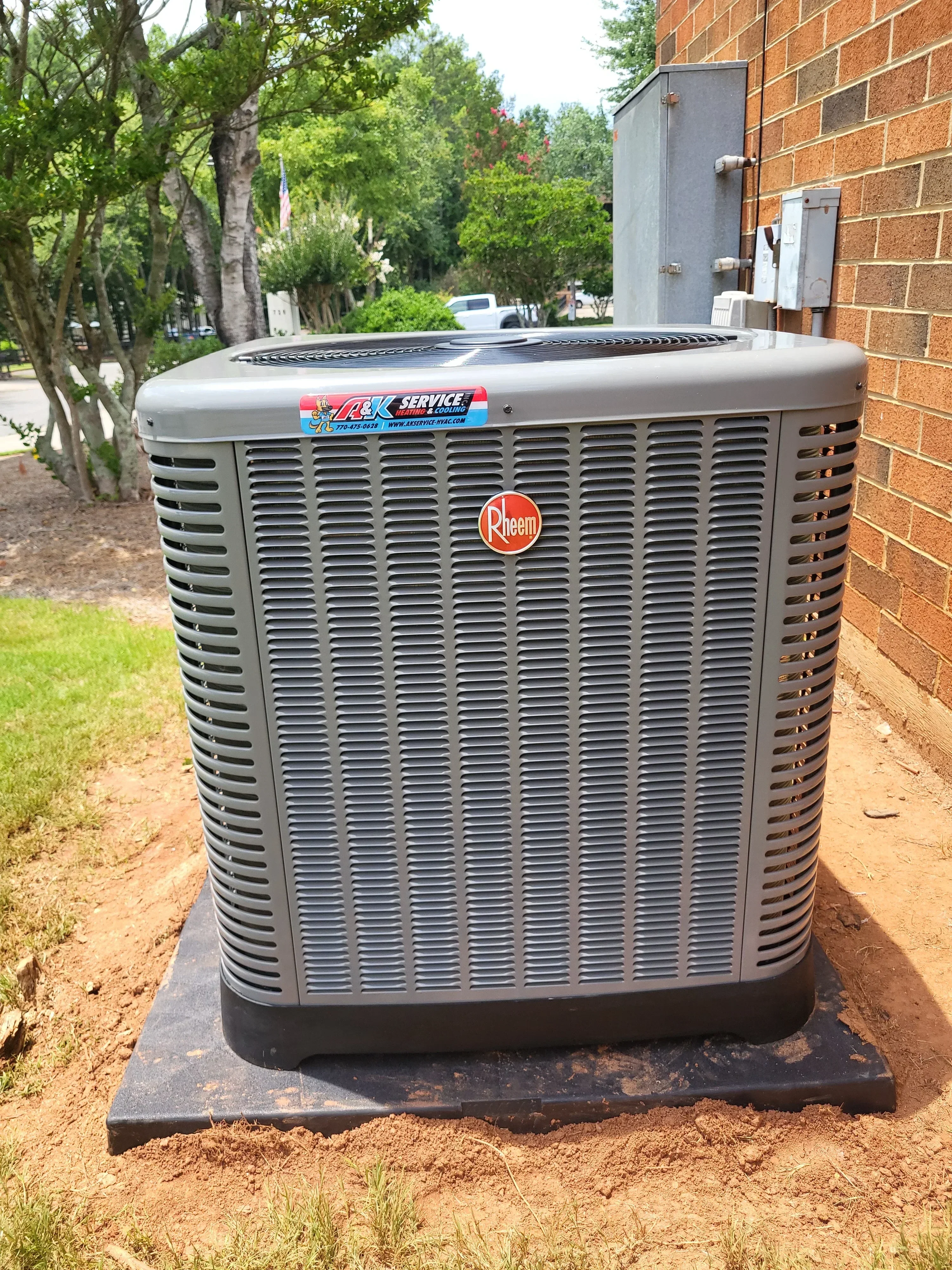 New air conditioning condenser unit installed on concrete pad against brick foundation