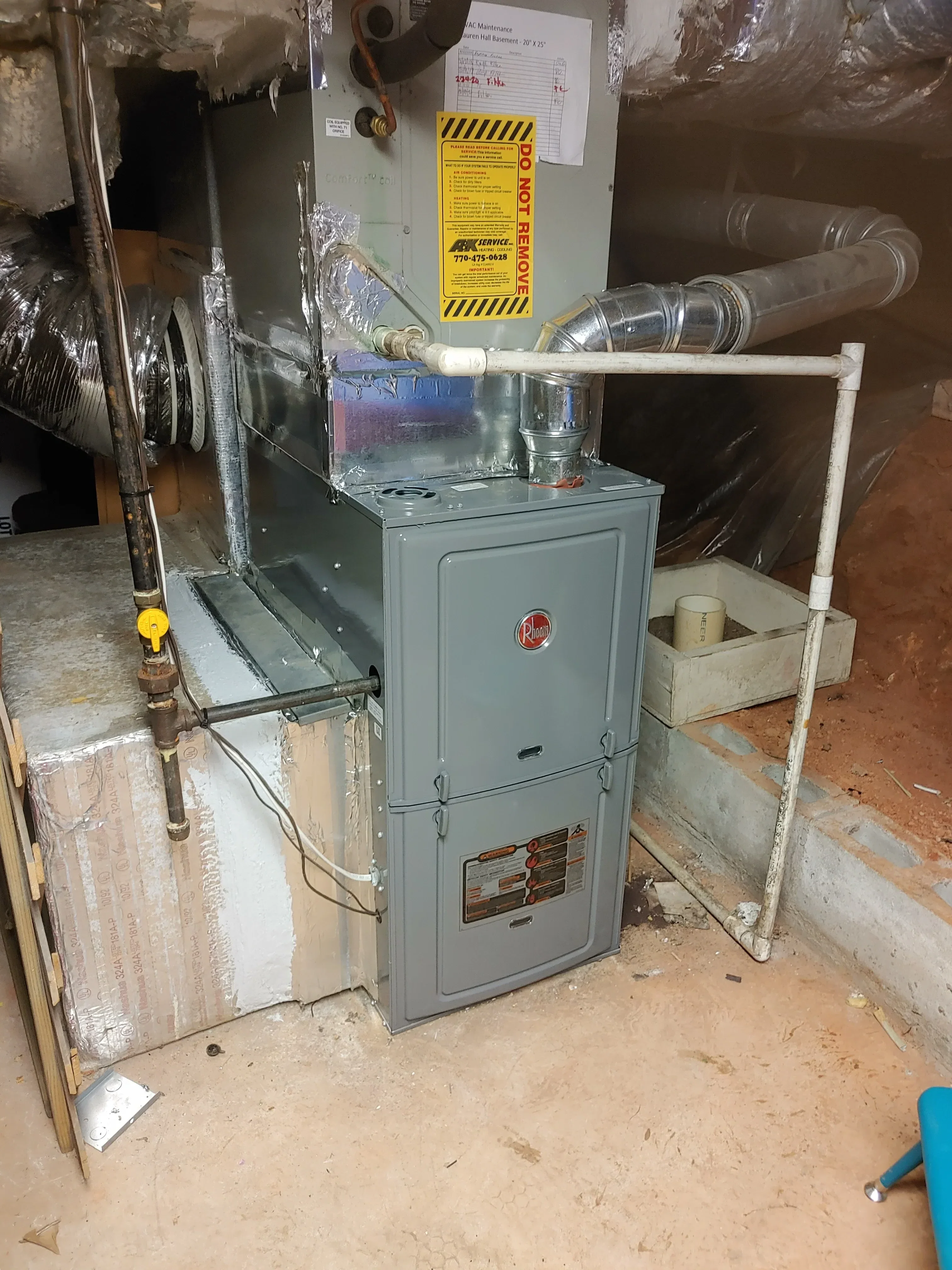 New furnace unit with metal ductwork, piping connections, and safety labels installed in basement