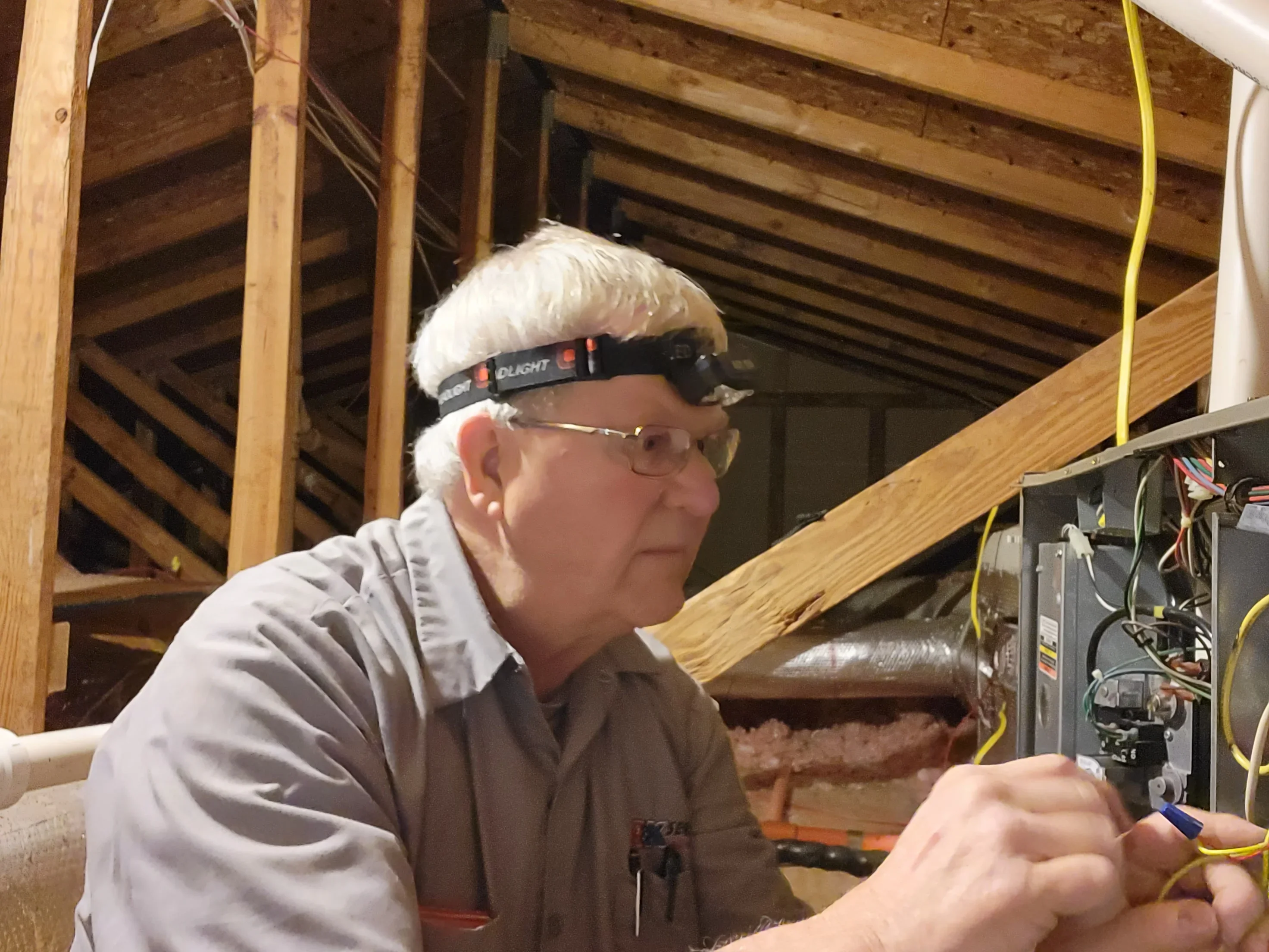 Technician installing HVAC equipment and yellow ductwork in wooden-framed attic space