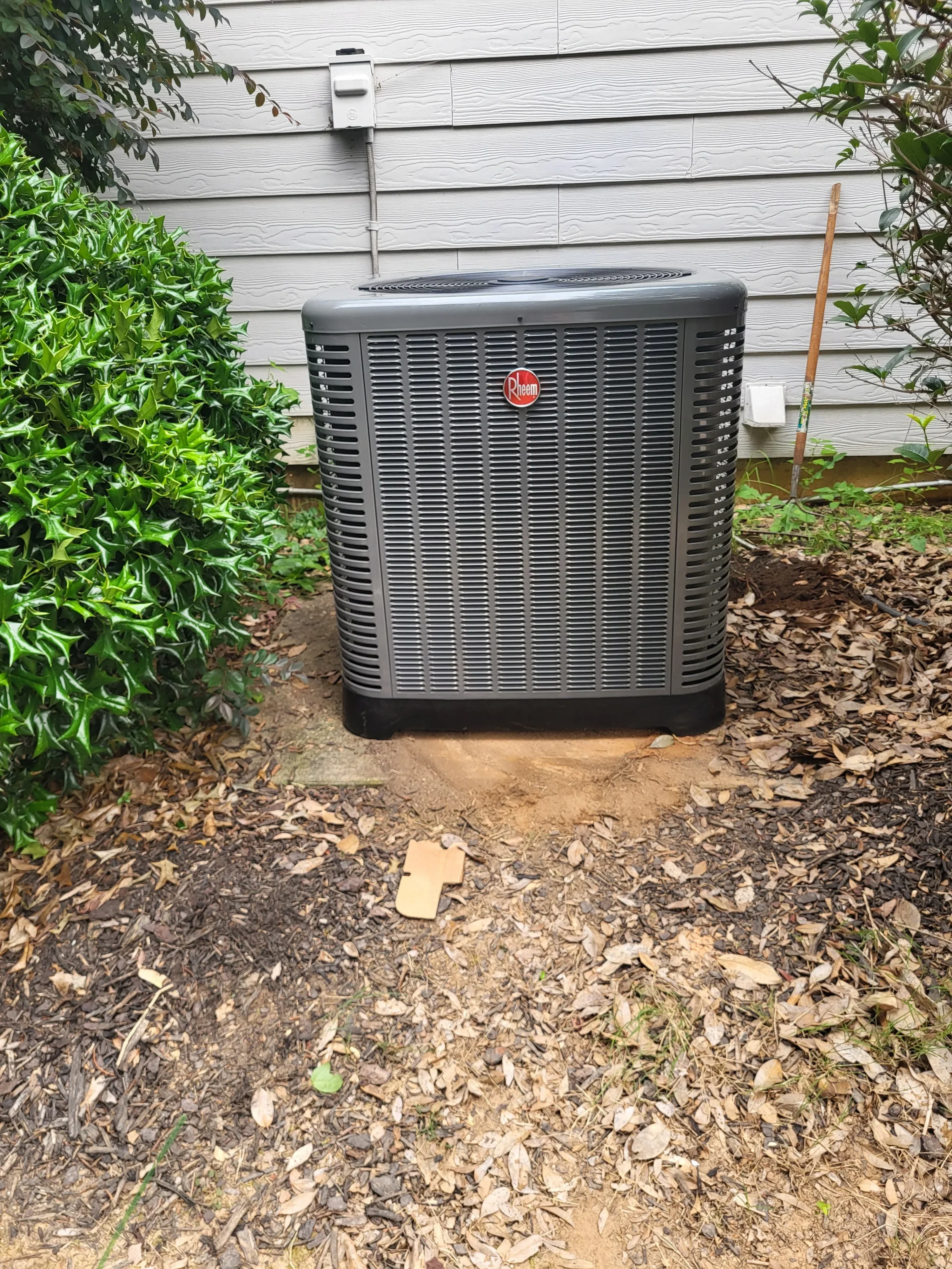 Black AC condenser unit installed on ground pad next to white vinyl siding