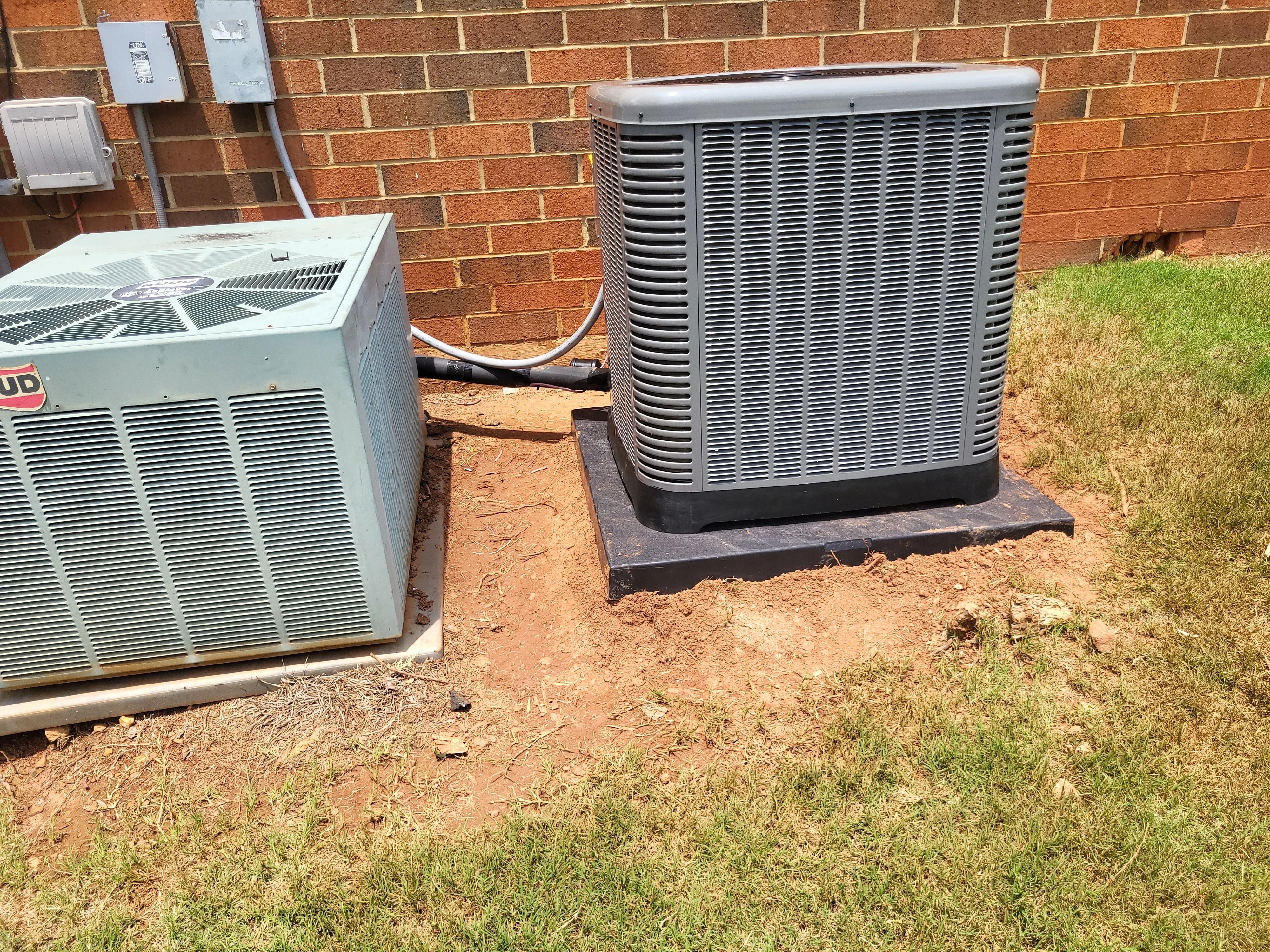 Two gray HVAC condenser units on concrete pads with connecting lines against brick wall